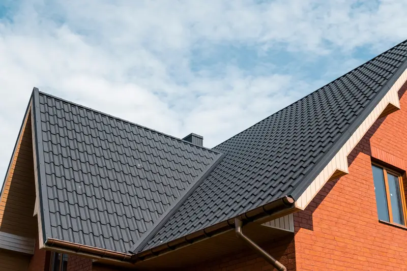 Dark grey pitched roof with guttering and a downpipe on a red brick house